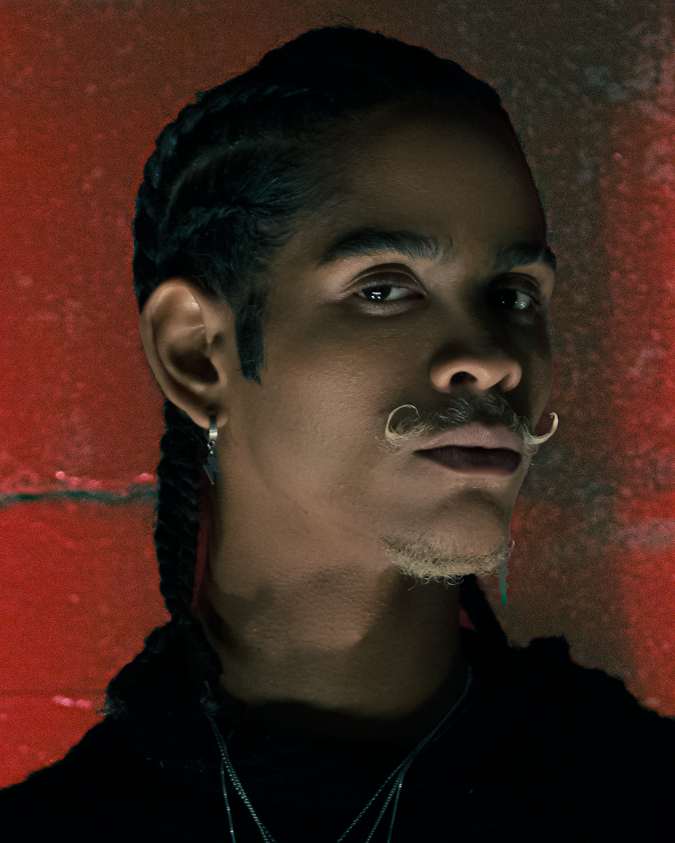 Close-up portrait of a stylish man with a unique moustache against a red background in São Paulo, Brazil.