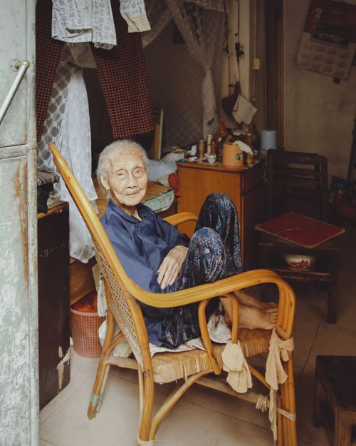 Free An elderly woman sits comfortably in a woven armchair inside a cozy room, exuding warmth and relaxation. Stock Photo