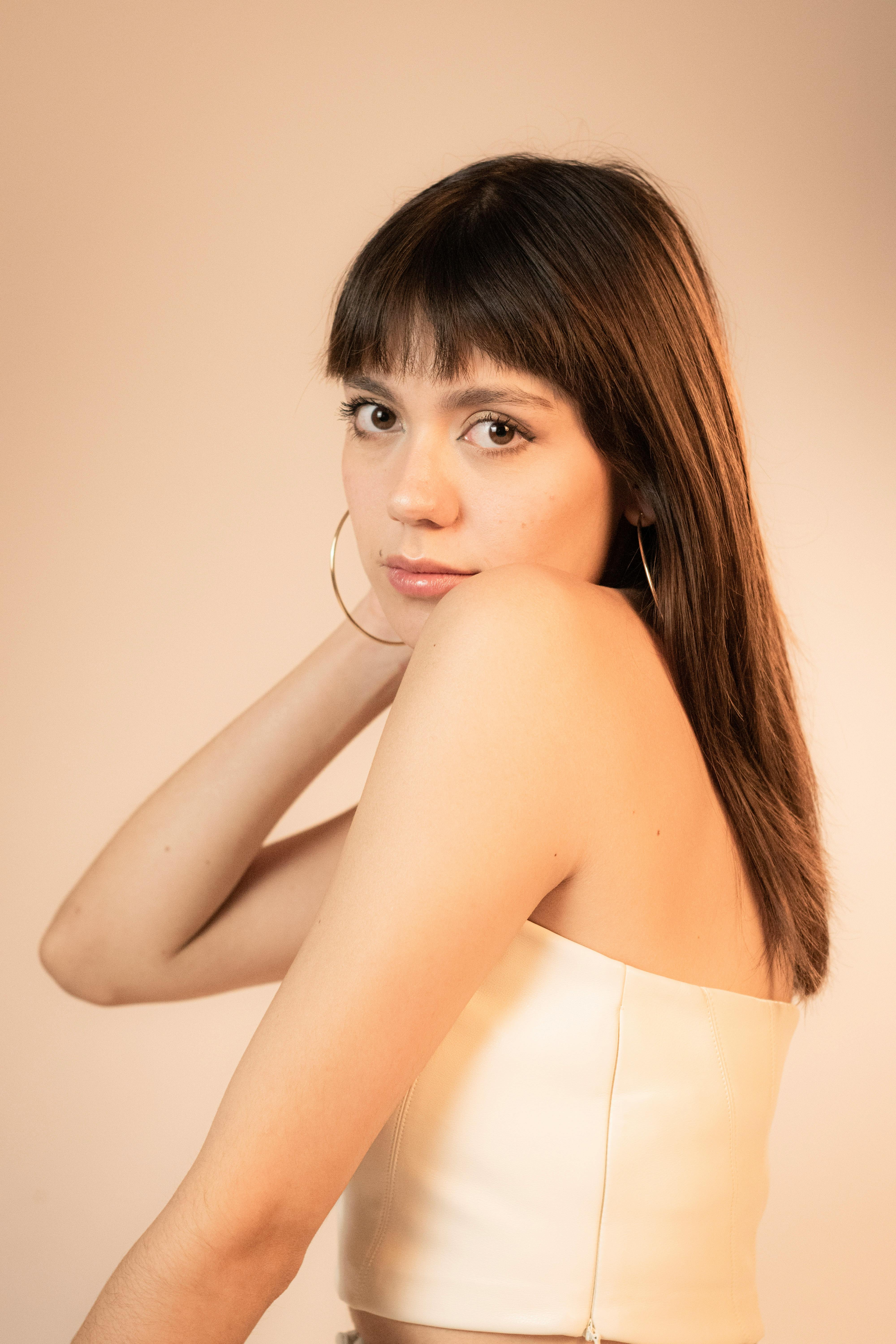 Chic studio portrait of a young woman with bangs, hoop earrings, and a strapless top.