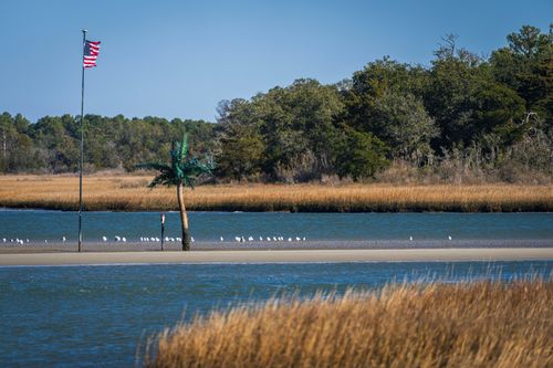 Free Picturesque scene of a sandbank with birds and an American flag in a serene coastal landscape. Stock Photo