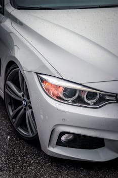 A detailed close-up of a white luxury car with rain droplets, parked outdoors.