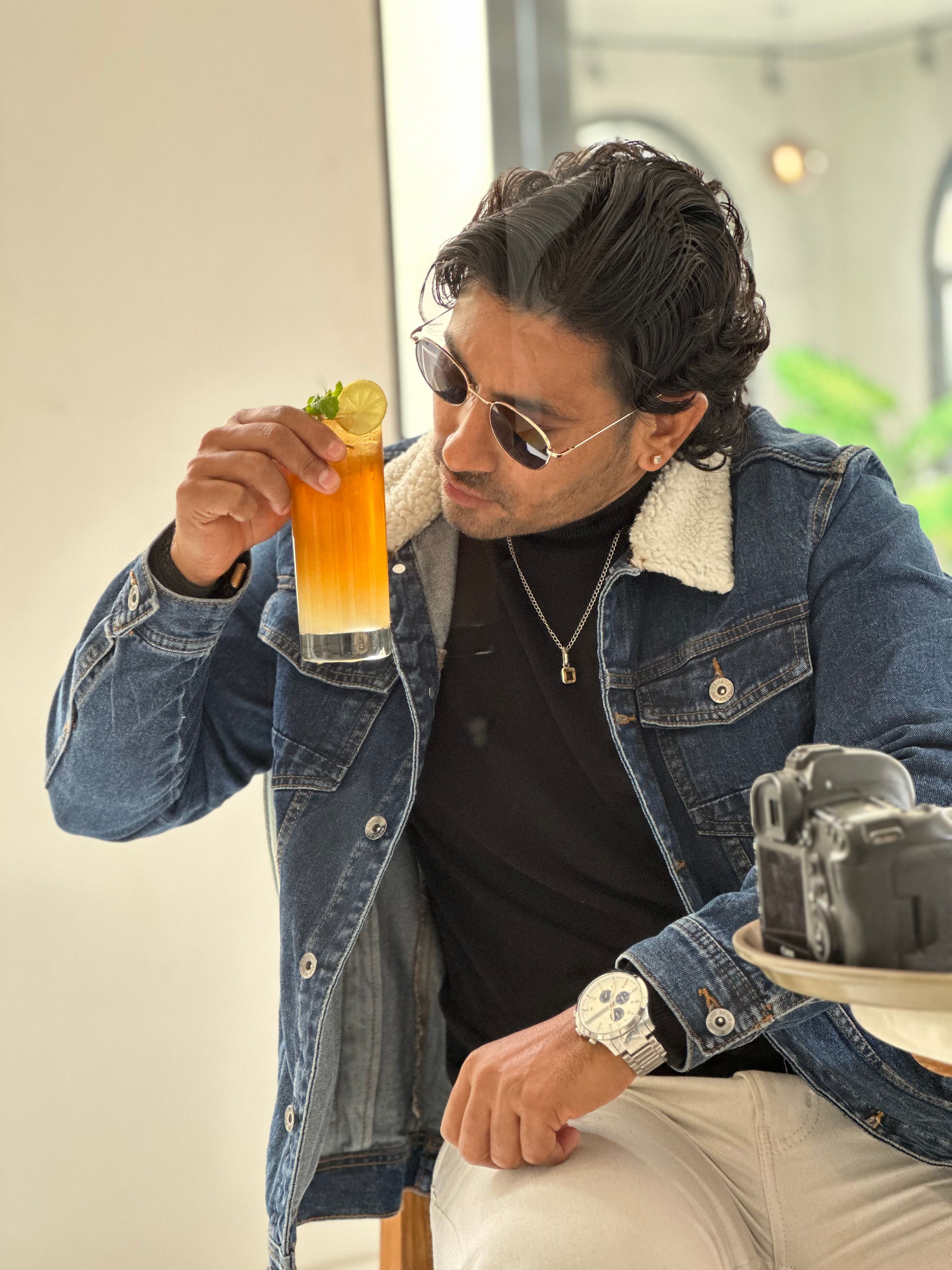 Man in sunglasses sipping a citrus cocktail while seated indoors in a casual setting.