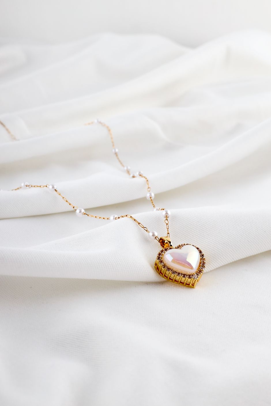 A gold heart pendant necklace arranged on white satin