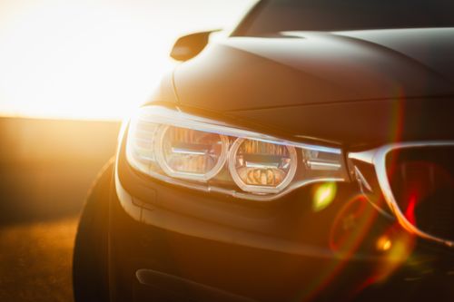 Free Sunlit close-up of a sleek modern car headlight with a lens flare effect at sunset. Stock Photo