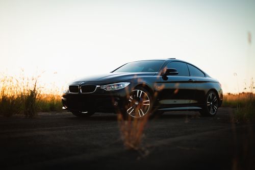 Free A modern black car parked at sunset in a serene field, highlighting its sleek design and polished exterior. Stock Photo