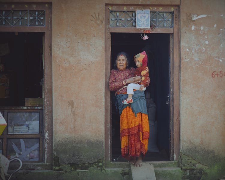 Grandma Standing With Grandchild In House Doorway