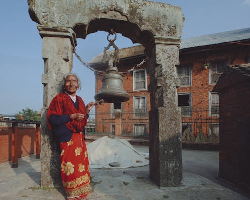Woman in Traditional Clothing near Temple Bell