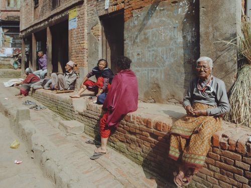 Free Elderly people sitting by a brick wall in a rural village setting. Daytime. Stock Photo