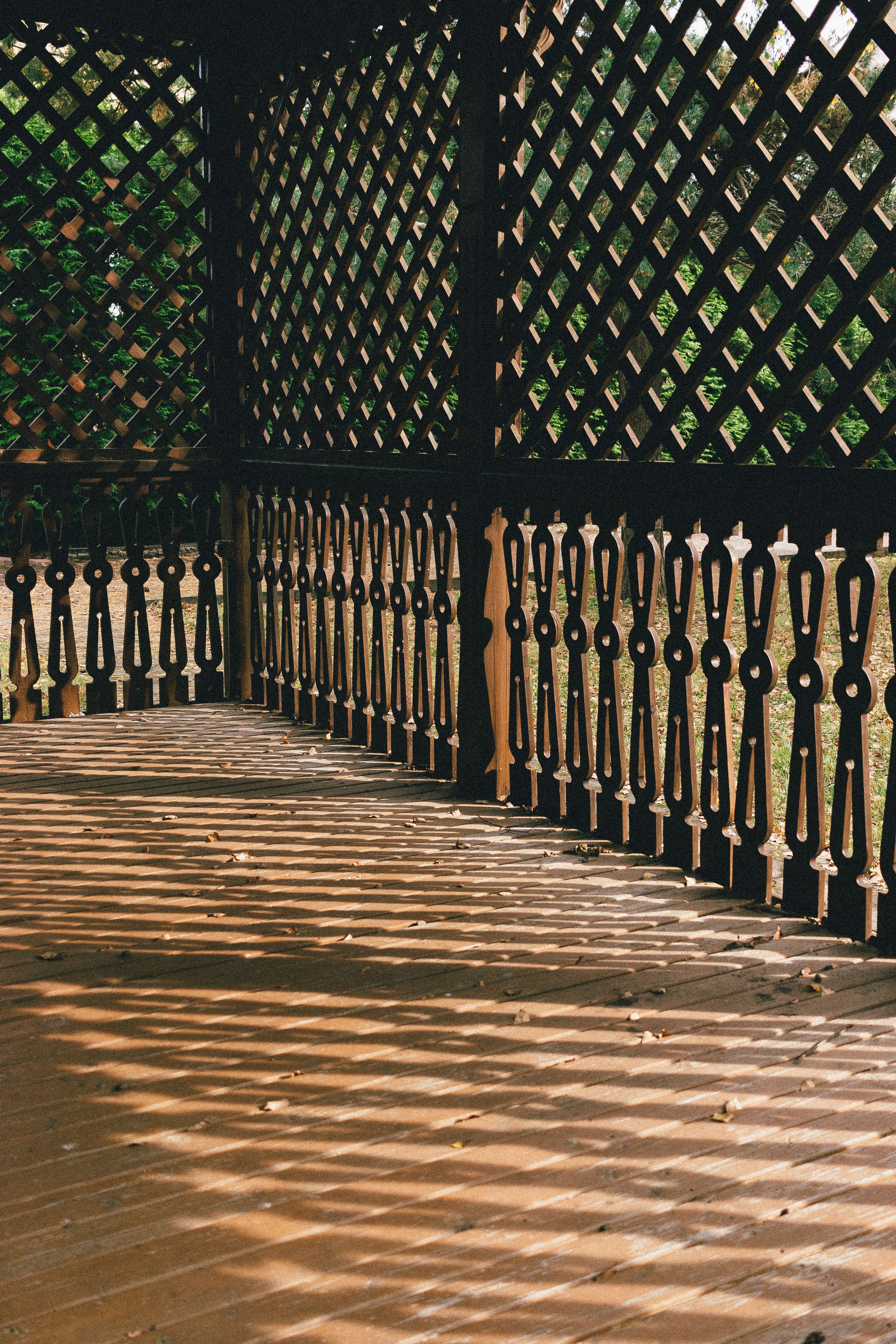 Sunlight creates intricate geometric patterns on a wooden patio, casting shadows through lattice fencing.