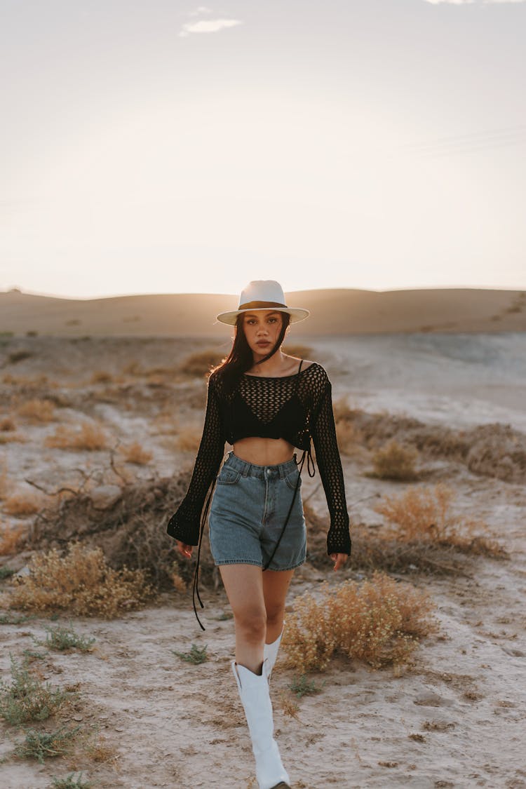 Young Woman In A Fashionable Outfit With Cowboy Boots Posing In The Desert 