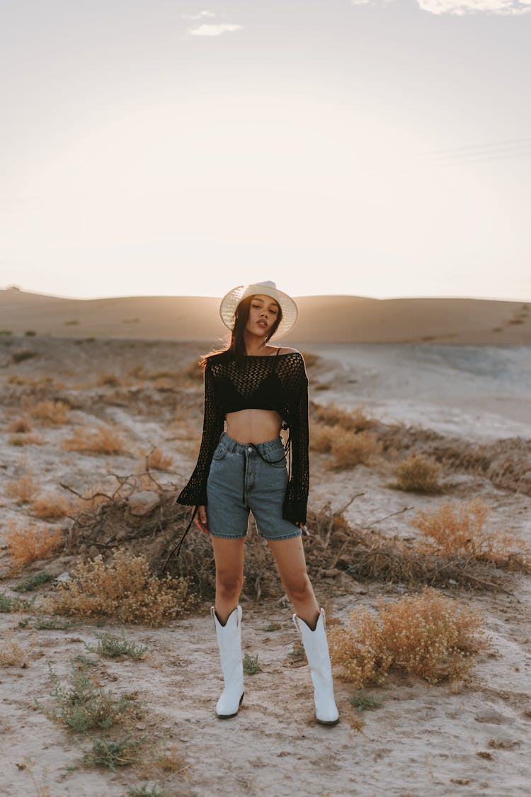 Young Woman In A Fashionable Outfit With Cowboy Boots Posing In The Desert 