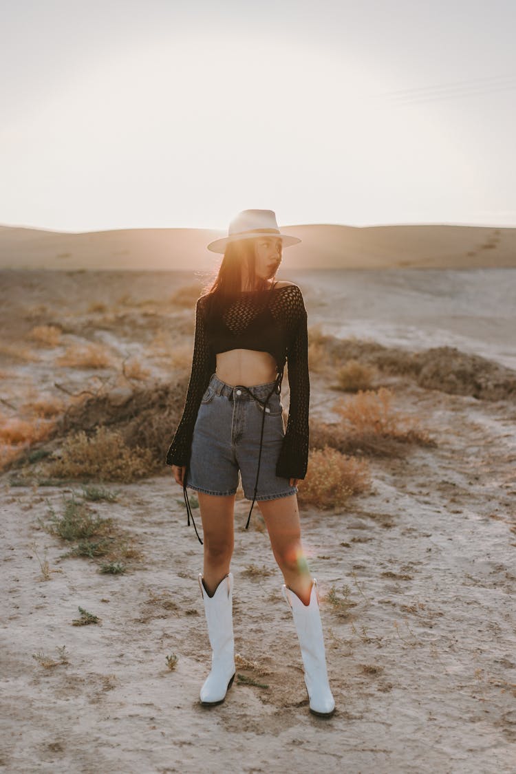 Young Woman In A Fashionable Outfit With Cowboy Boots Posing In The Desert 