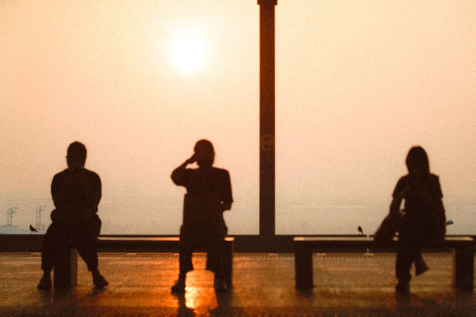 霞んだ夕日を背景にベンチに座る人々のシルエット。