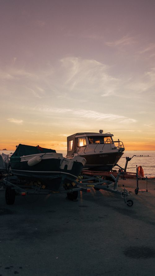 Free Boats on trailers at the seaside under a vibrant sunset sky. Stock Photo