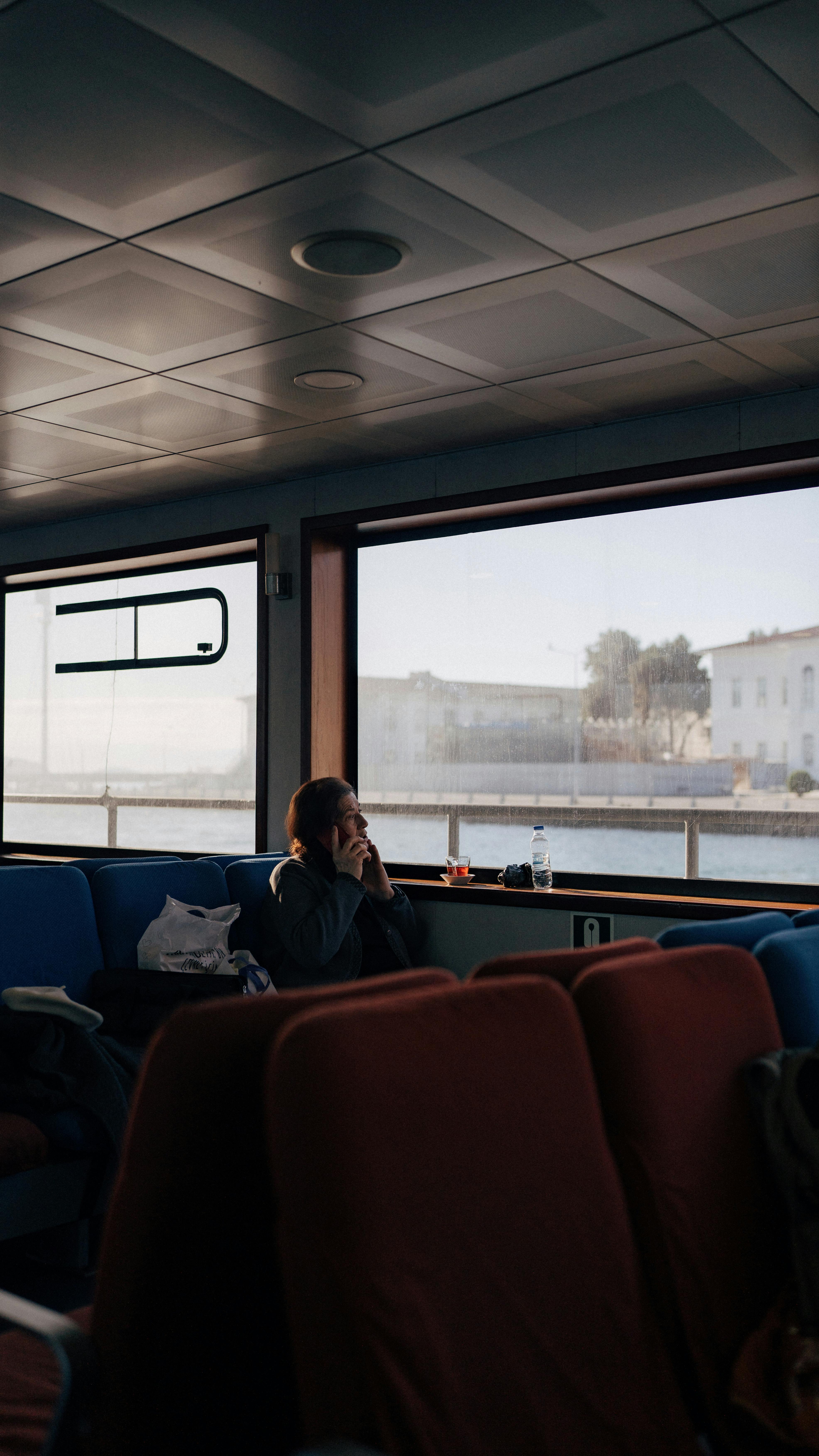 A woman on a ferry sits by the window, gazing outside, capturing a serene travel moment.
