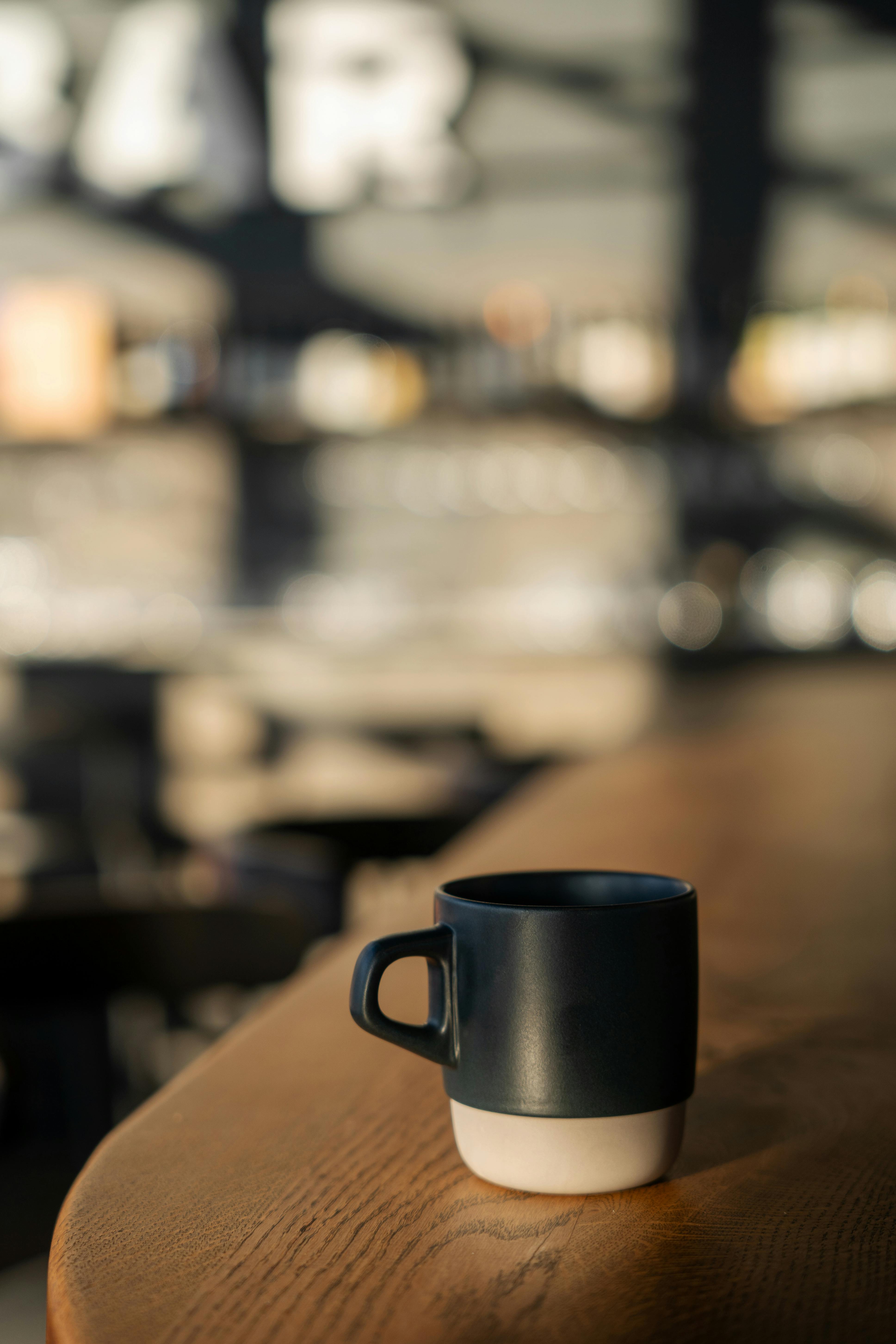 A black and white cup on a wooden table with a blurred cafe background, capturing warm morning light.