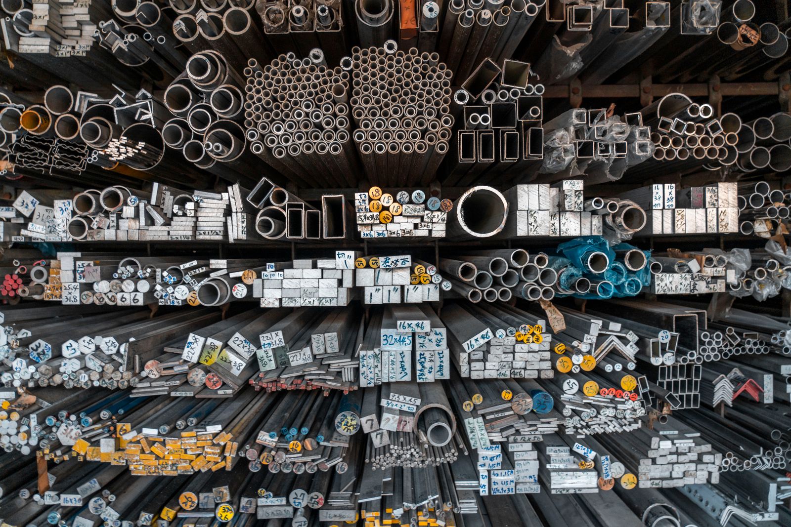 Racks of structural steel sections — angles, channels, flats, pipes and rounds sorted by size