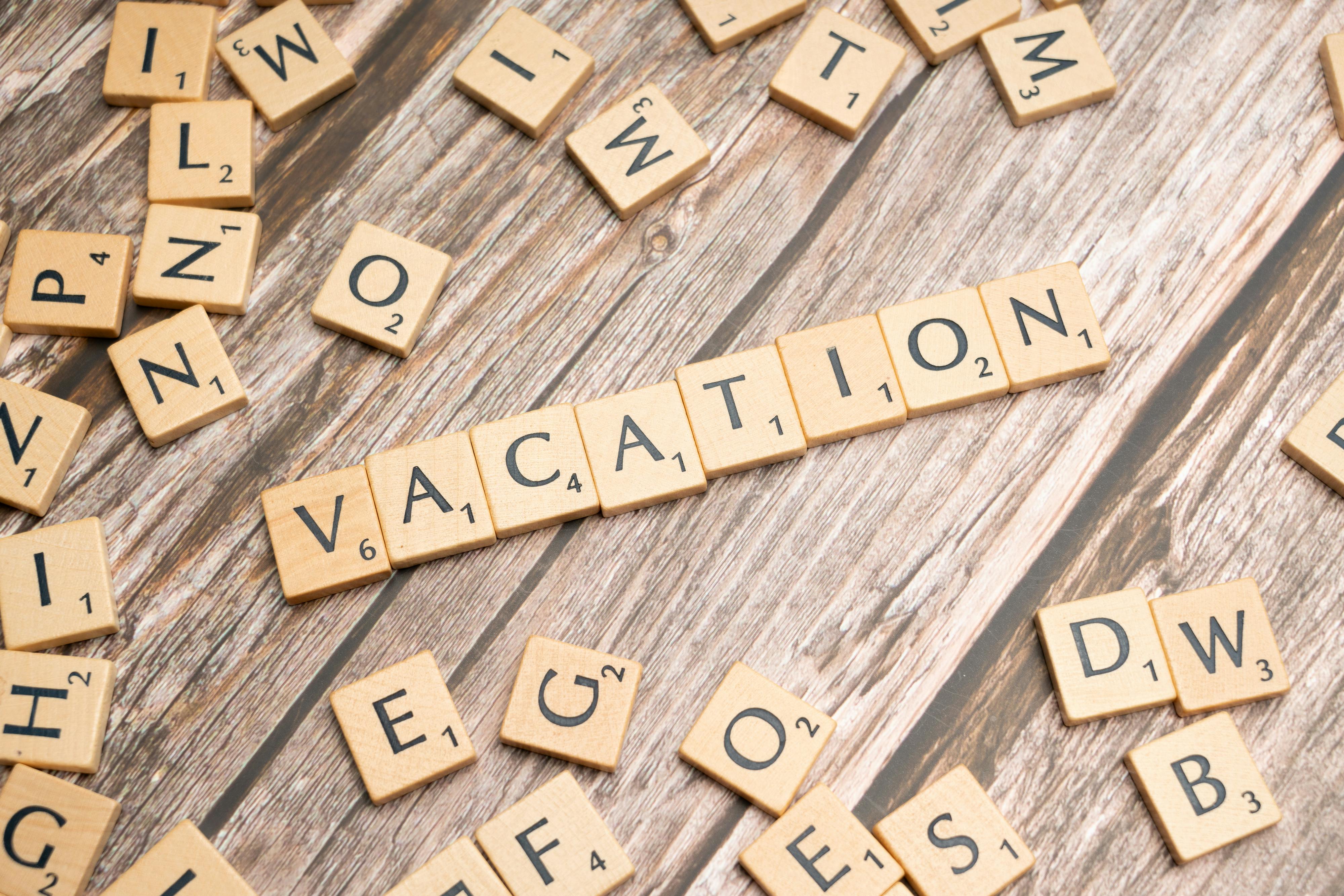 Wooden Scrabble tiles form the word 'Vacation' on a rustic wooden background, symbolizing leisure and travel.