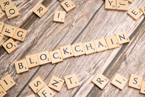 Free Wooden letter tiles form the word 'blockchain' arranged on a rustic wood background. Stock Photo