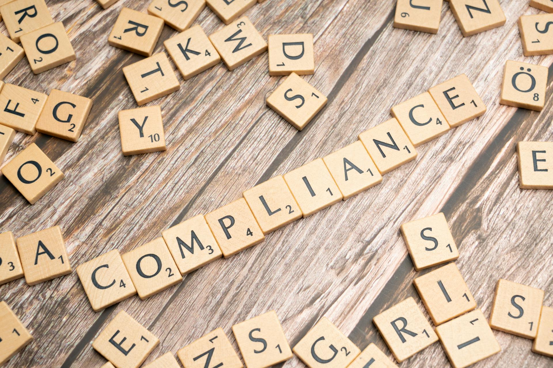 Wooden letter tiles forming the word 'COMPLIANCE' on a rustic wooden background.