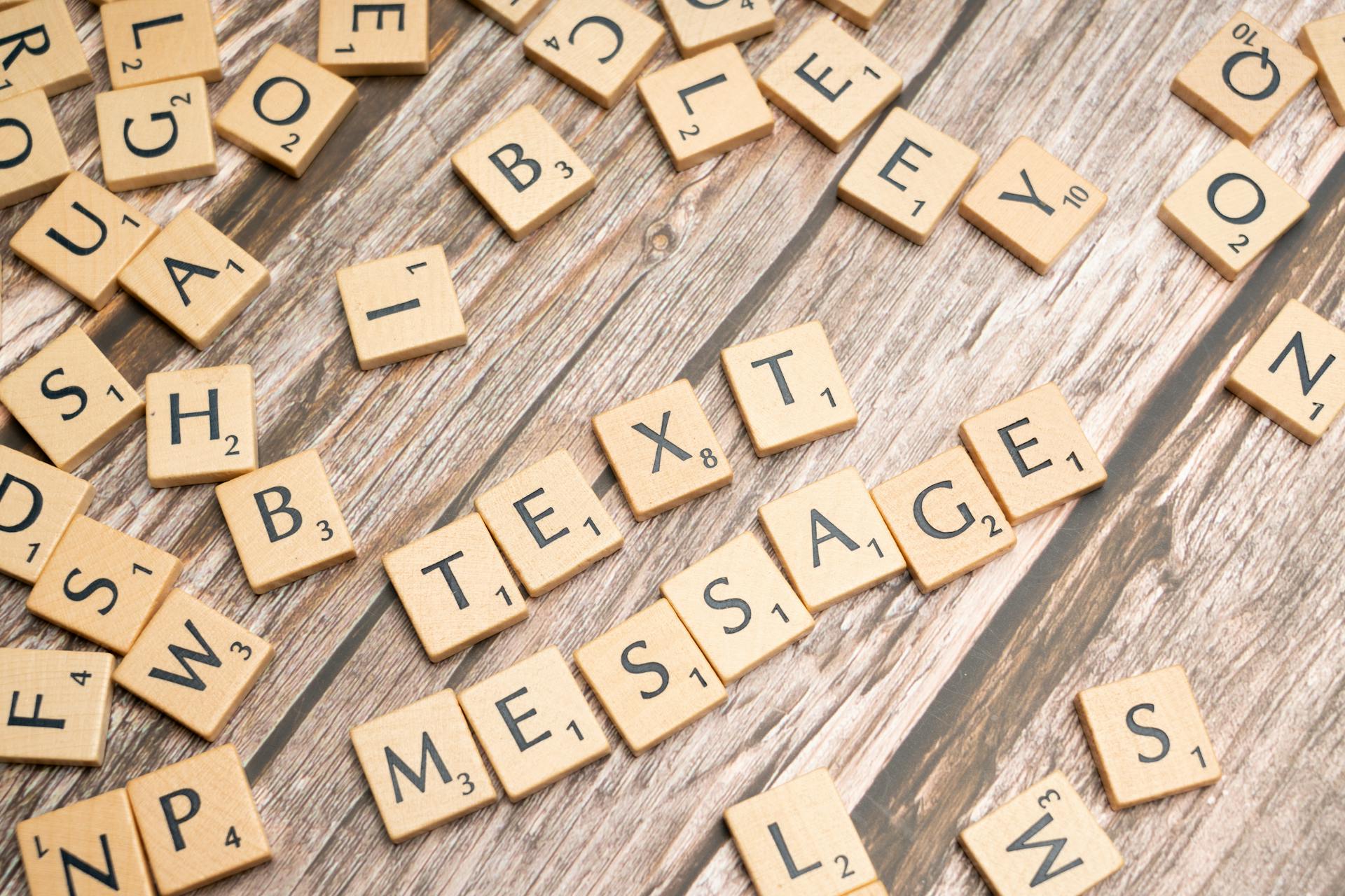 Wooden letter tiles arranged on a wooden surface spelling out 'TEXT MESSAGE'.