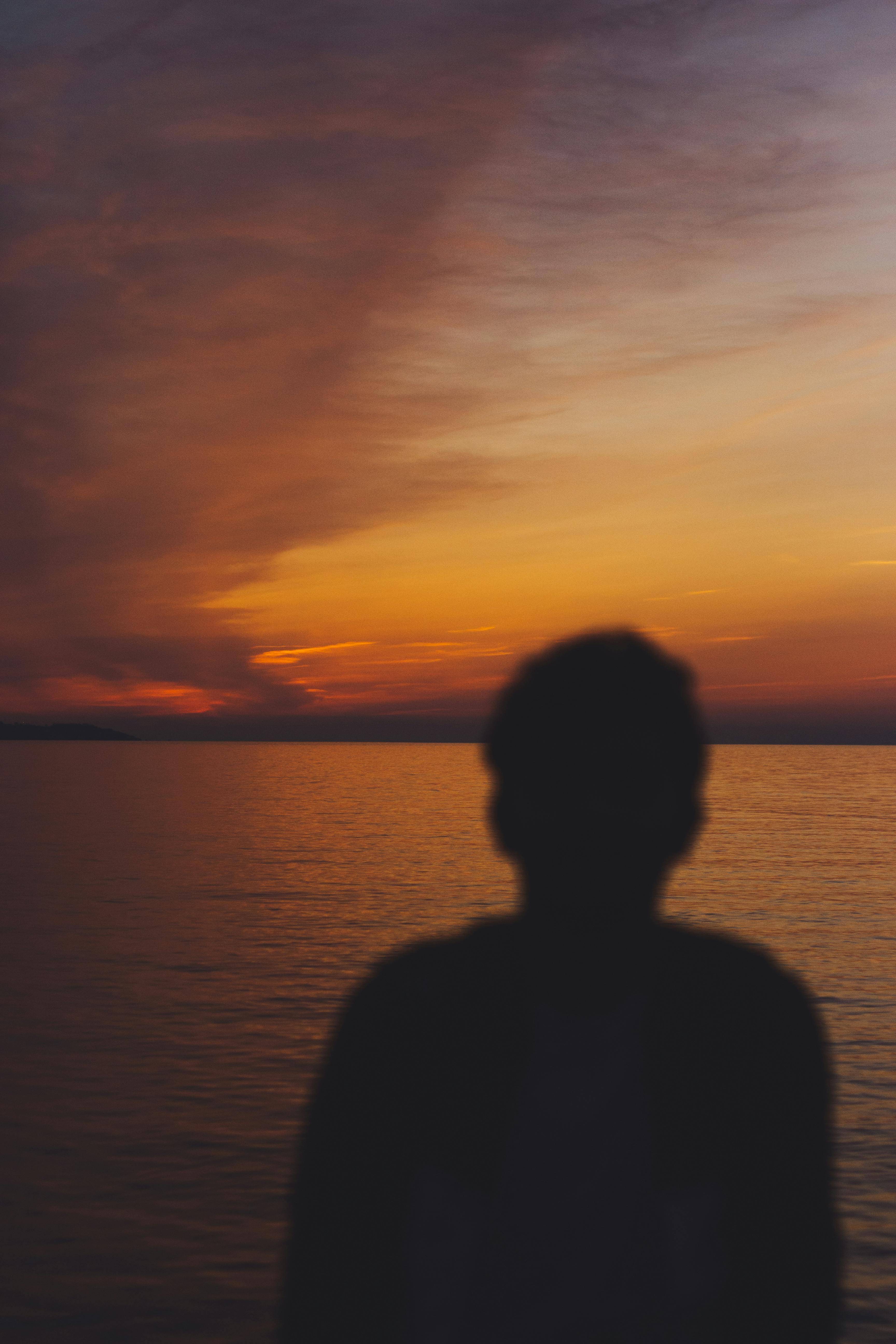 Silhouette of a man by the sea with a captivating sunset backdrop. Perfect for serene and contemplative themes.