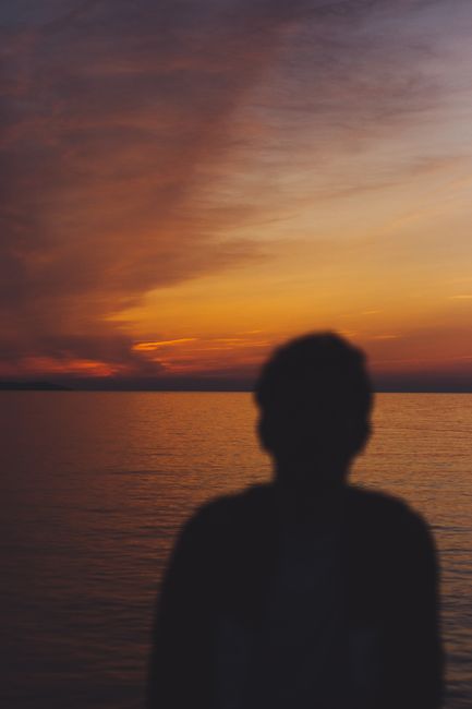 Silhouette of a man by the sea with a captivating sunset backdrop. Perfect for serene and contemplative themes.