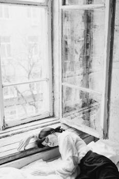 A woman rests on a windowsill, captured in monochrome artistry
