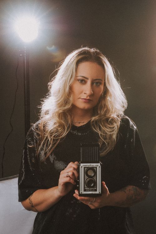 Free Blonde woman posing with a vintage camera in a studio spotlight. Stock Photo