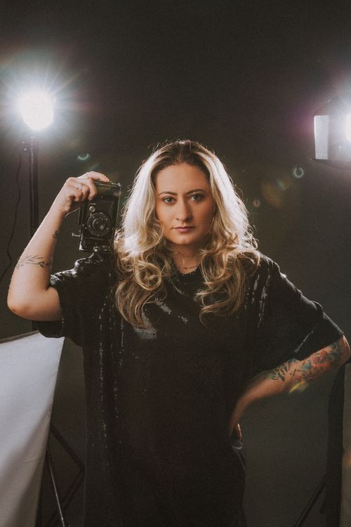 Free Blonde woman in black dress posing with a vintage camera in a studio setting. Stock Photo