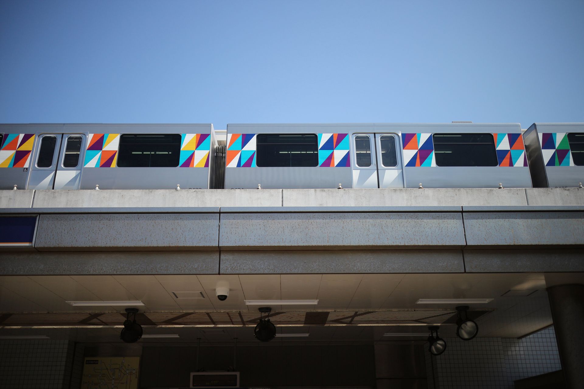 Vibrant patterned train on elevated track in Yokohama, Japan against a blue sky.