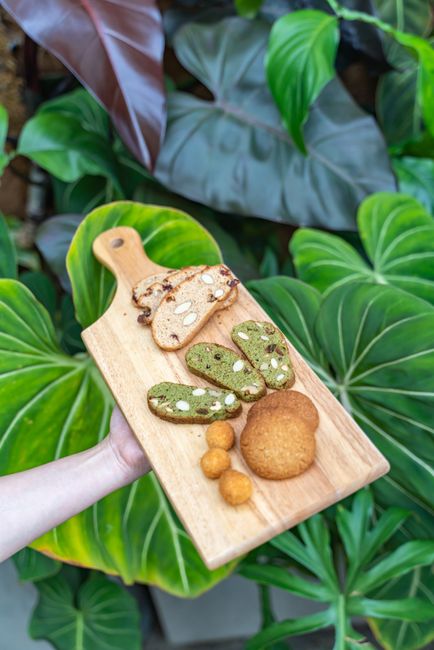 Delicious artisan cookies displayed on a wooden tray, held against a backdrop of vibrant green foliage.