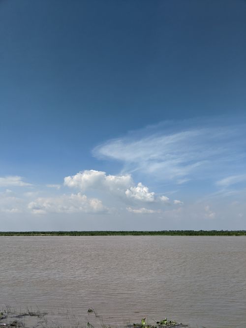 Free Tranquil river scene with lush greenery and a clear blue sky in Tanda, India. Stock Photo