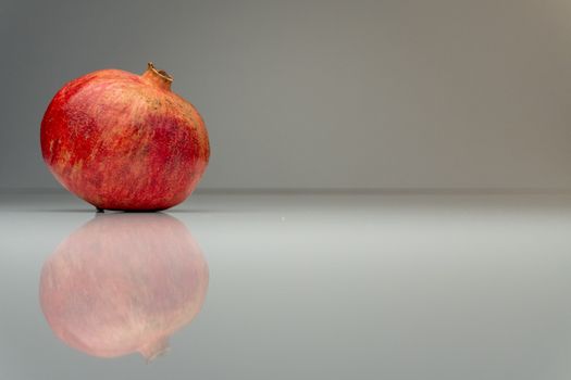 A single pomegranate reflected on a sleek gray surface, perfect for minimalist themes.
