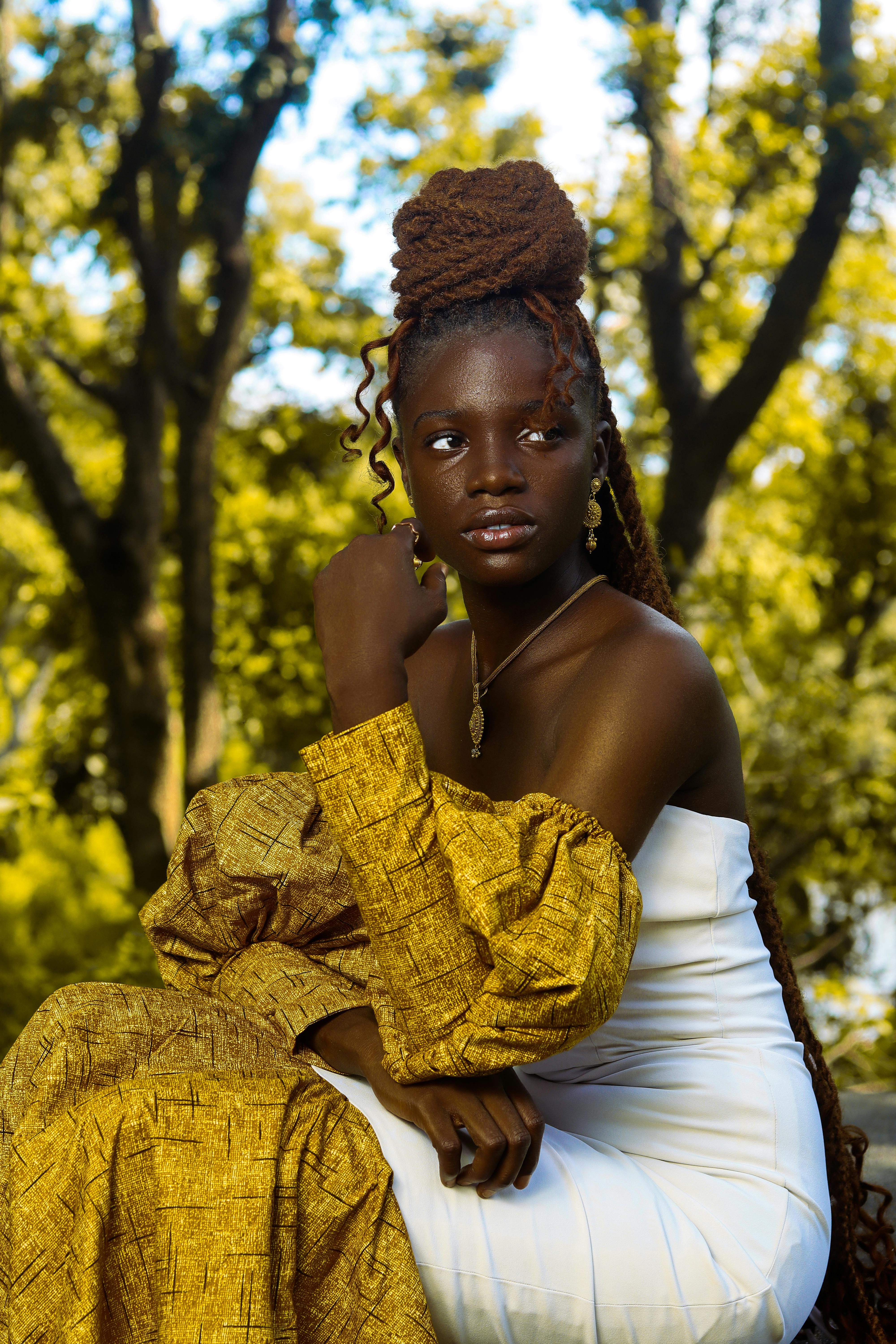 Striking outdoor portrait of a woman in a stylish yellow and white outfit with natural lighting.