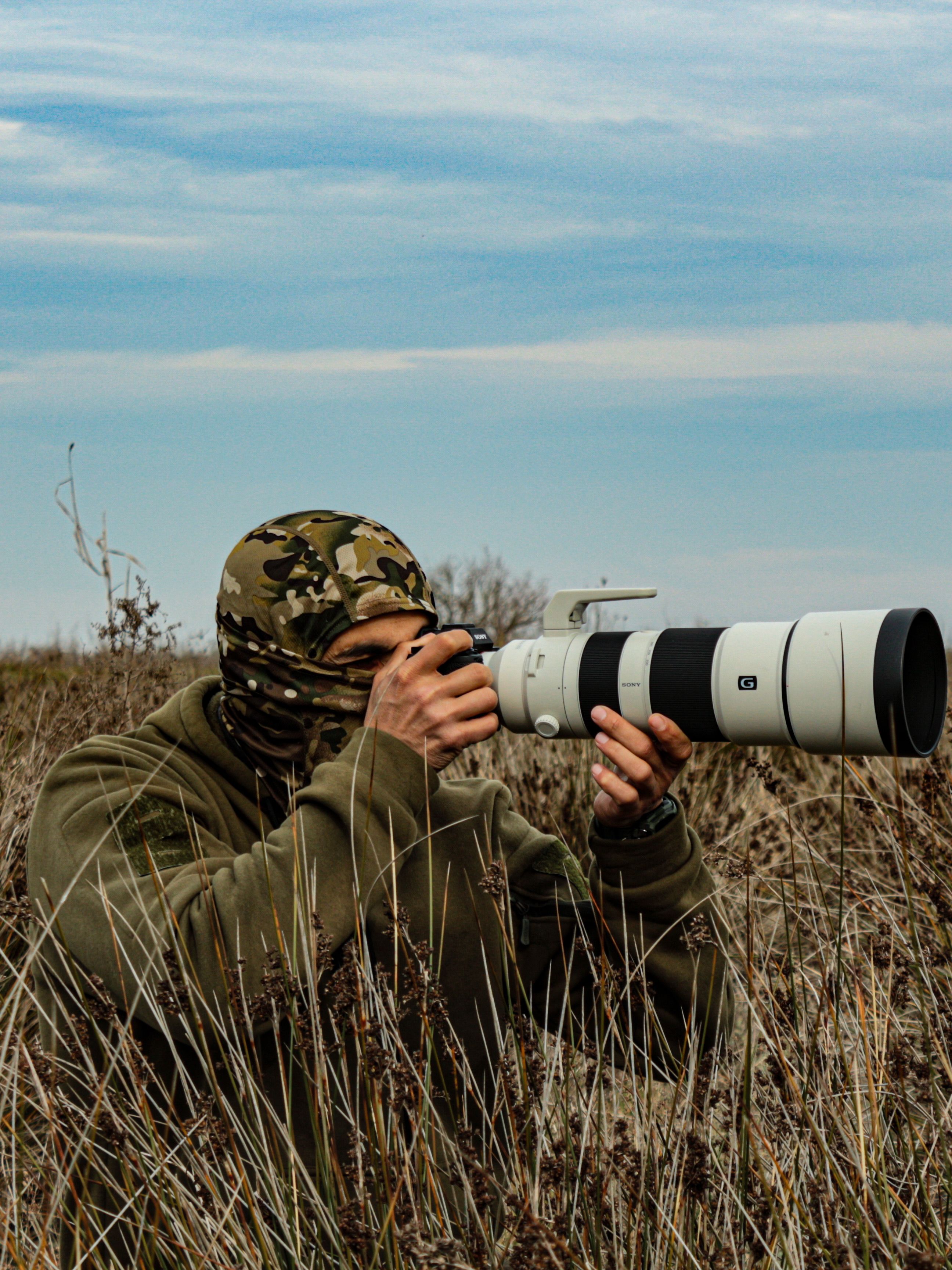 Camouflage-clad photographer capturing wildlife with a telephoto lens in a rural field.