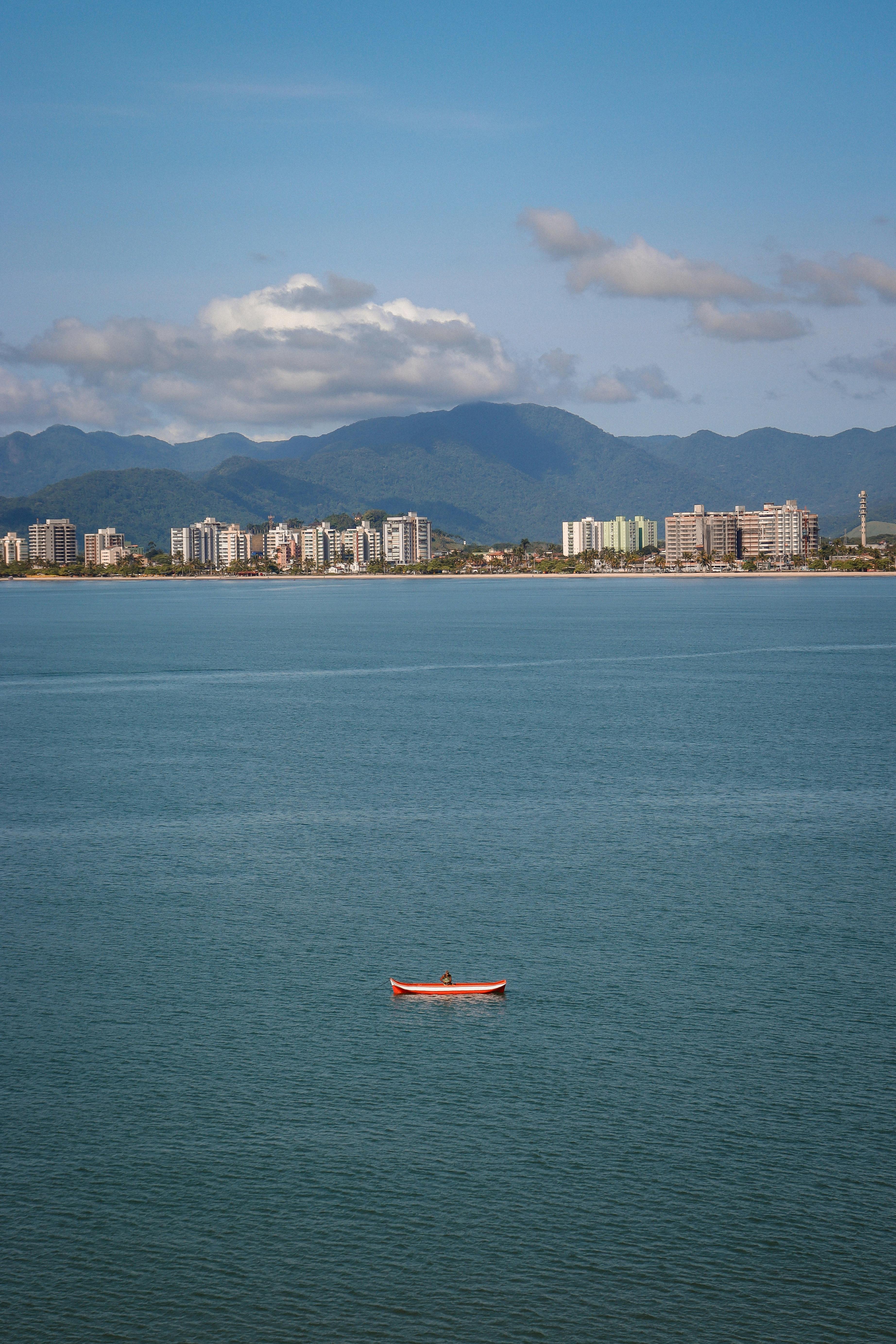 Scenic aerial view of urban skyline across a calm sea with red boat in foreground.