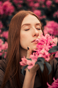 一位闭目养神的女子，正享受着户外粉红花朵的芬芳