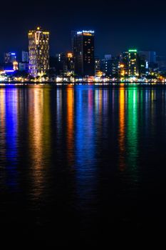 Colorful city skyline reflecting on the river at night, illuminated buildings and glowing nightlife.
