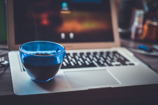 A blue glass cup with a warm beverage on an open laptop, blending technology and relaxation.