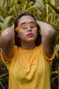 一名蒙着眼睛、身穿黄色衬衫的年轻女子站在户外的植物丛中