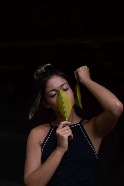 Artistic portrait of a young woman holding leaves against a dark background.