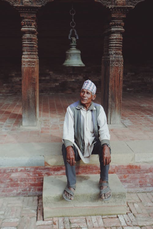 Senior Man Sitting in Front of a Temple Bell