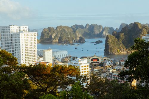 Free View of Ha Long Bay with tall buildings and iconic limestone karsts at sunrise. Stock Photo