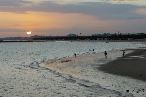 Free Peaceful sunset at the beach with people enjoying the serene shore and gentle waves. Stock Photo