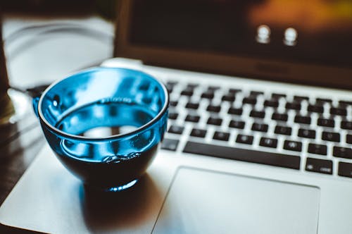 銀のラップトップコンピューター上の青いガラスカップの浅い焦点写真