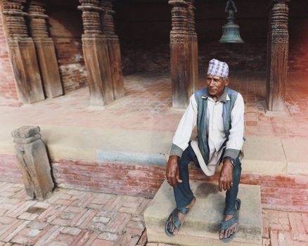 Portrait of a senior man sitting on steps in a traditional Nepali setting, showcasing cultural attire.
