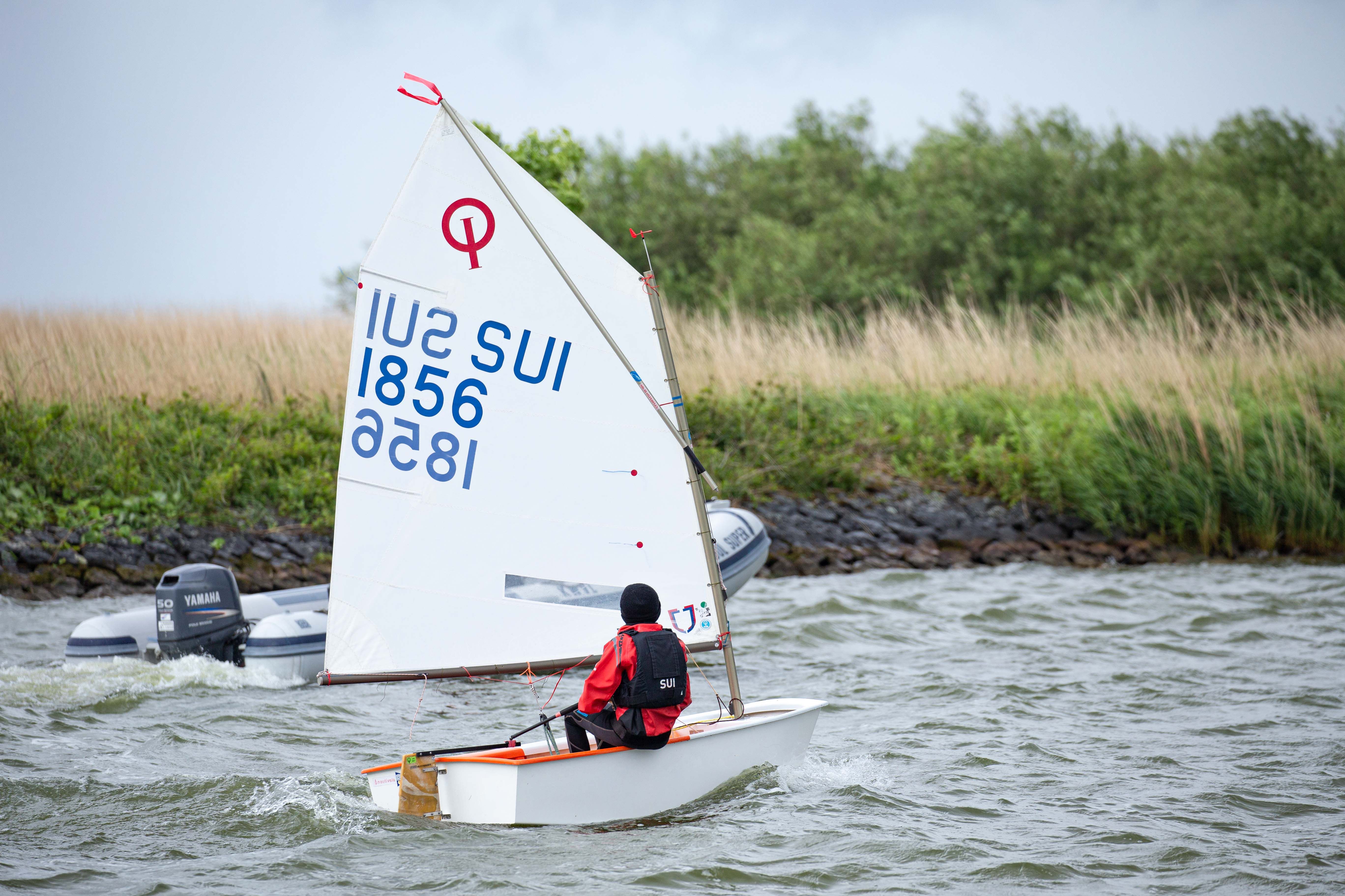 A sailor skillfully navigates a small sailboat during a race on a windy day.