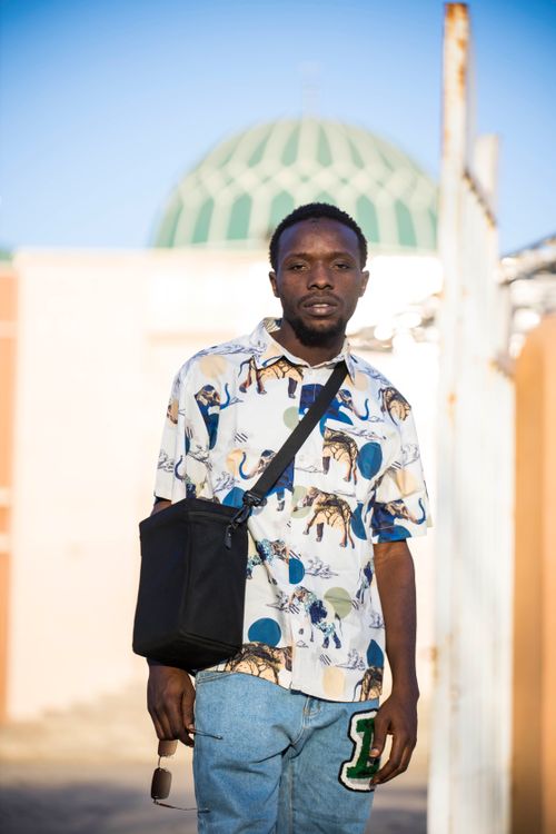 Free Young man standing outside near a mosque with a green dome, showcasing a casual outfit. Stock Photo