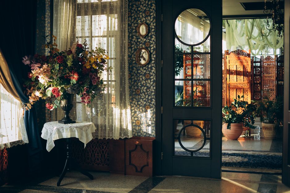Maximalist decor style interior — A vintage-styled room with a colorful floral bouquet and ornate door, bathed in warm sunlight.